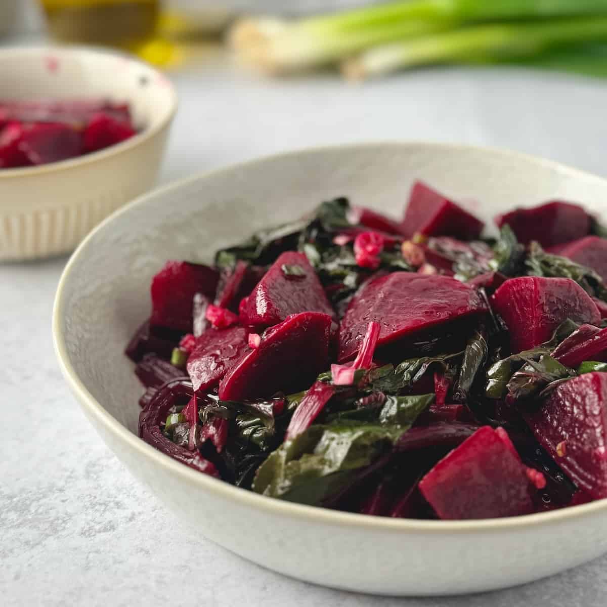 Greek beet salad served on a white bowl with green onions and olive oil bottle in the background.
