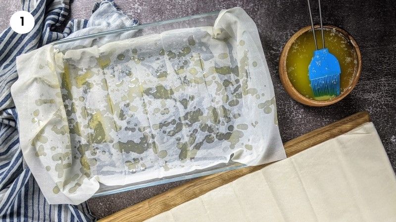 Adding the first layer of phyllo pastry to the bottom of the tray.