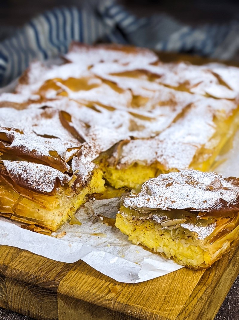 Greek custard pie with pumpkin dusted with powdered sugar and cinnamon on a wooden board.