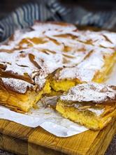 Greek custard pie with pumpkin dusted with powdered sugar and cinnamon on a wooden board and one slice cut.