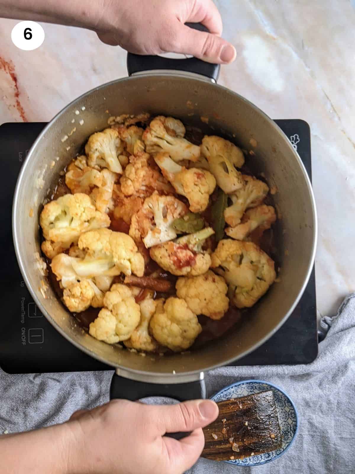Stirring the braised cauliflower by holding the pot handles.