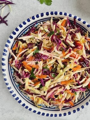 Greek cabbage salad served in bowl with cabbage slices and parsley next to the plate.