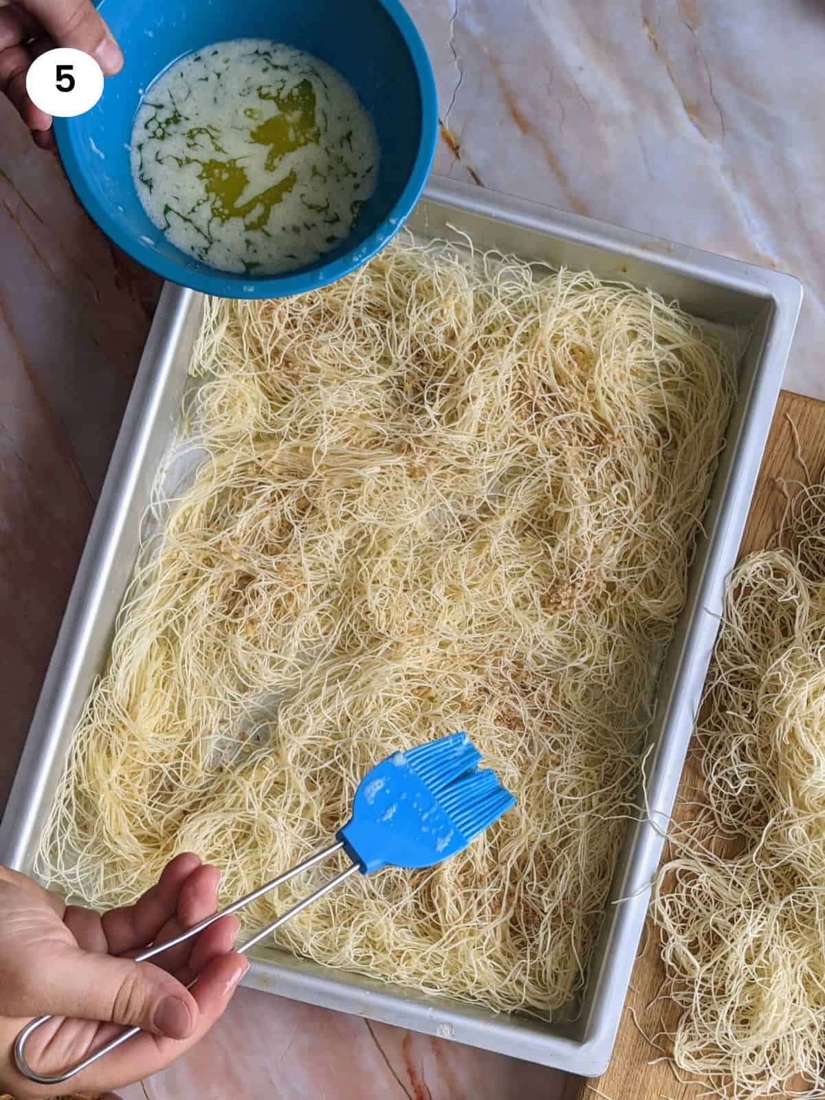 Drizzling the kataifi dough with butter.