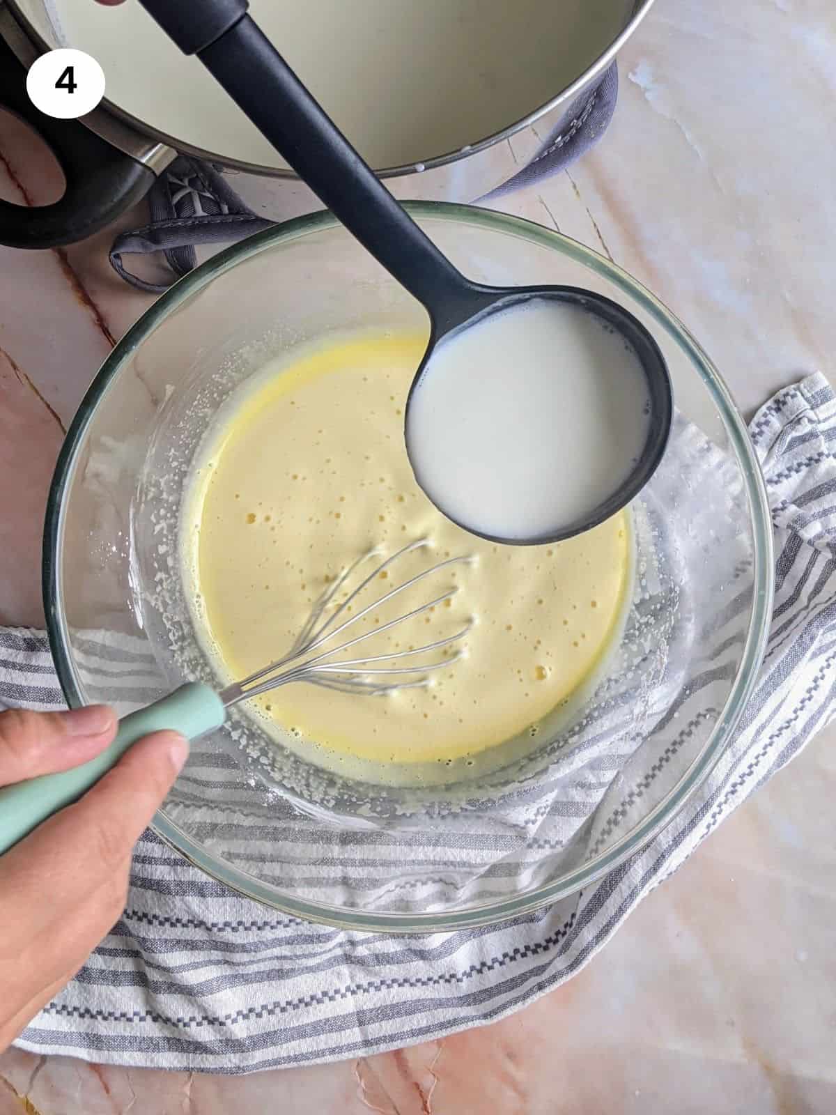 Ρίχνοντας το γάλα σιγά σιγά στη κρέμα με τα αυγά, ζάχαρη και κορνφλάουερ.
