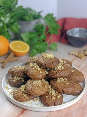 Melomakarona Greek honey cookies served on a white plate with an orange, walnuts and cinnamon sticks on the background.