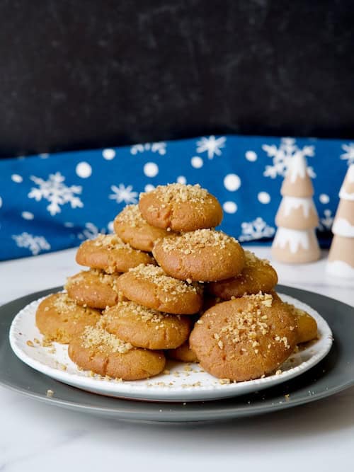 Melomakarona Greek honey cookies served on a white plate with an orange, walnuts and cinnamon sticks on the background.