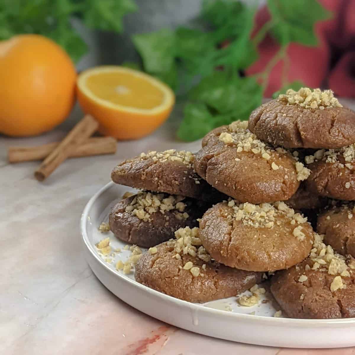 Melomakarona Greek honey cookies served on a white plate with an orange, walnuts and cinnamon sticks on the background.