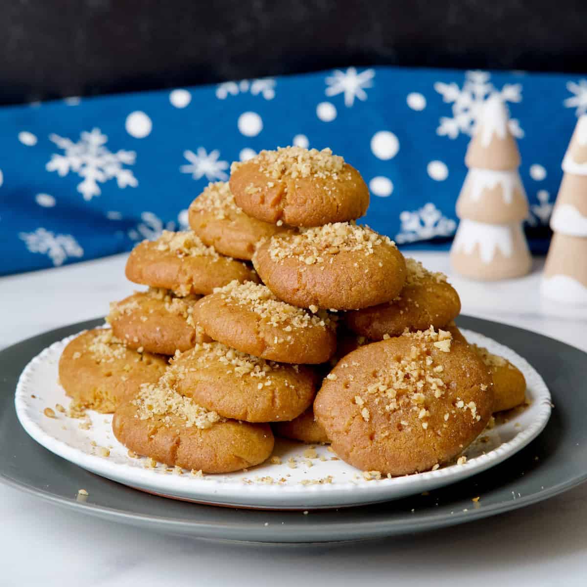 Melomakarona Greek honey cookies served on a white plate with an orange, walnuts and cinnamon sticks on the background.