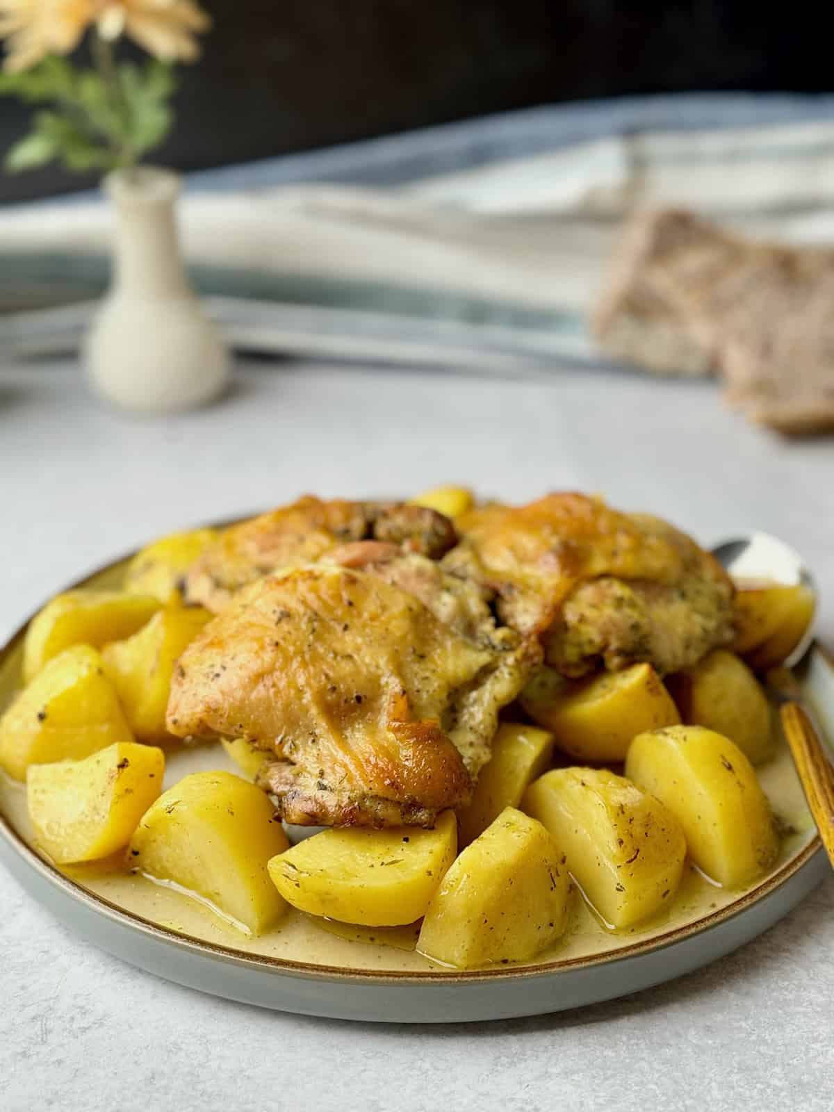 Greek roasted chicken thighs served on white plate with bread slices at the back.