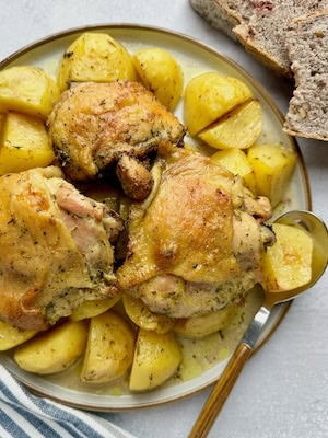 Chicken with potatoes served on plate with bread slices at the back.