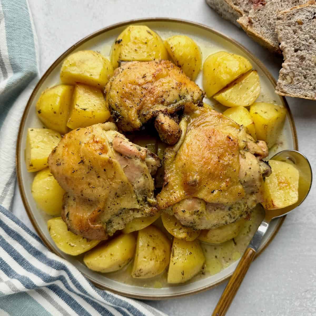 Chicken with potatoes served on plate with bread slices at the back.