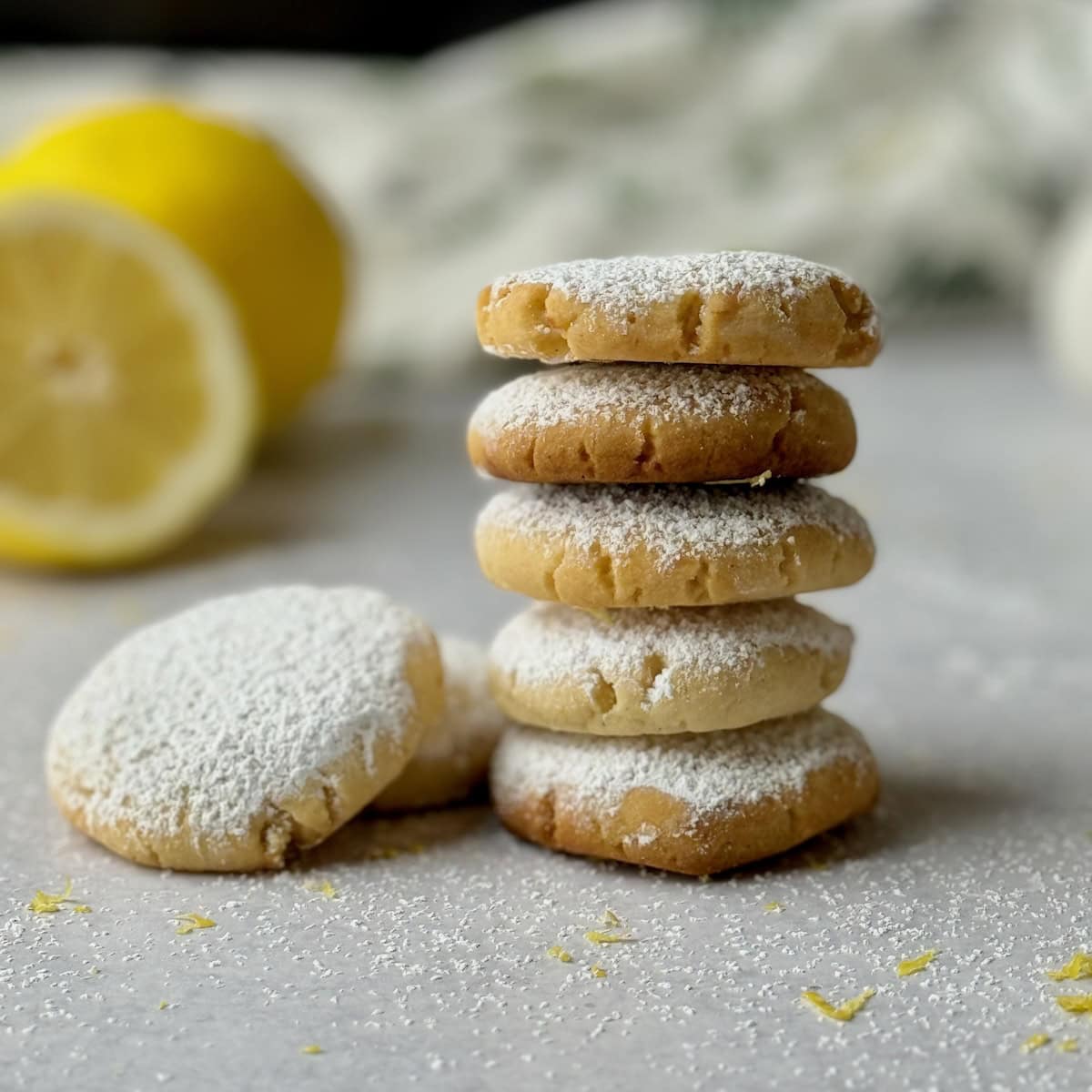 Greek lemon cookies in a stack with lemon in the background.