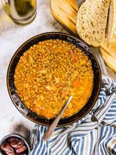 Mediterranean lentil soup served in black bowl next to olives and loaf of bread.