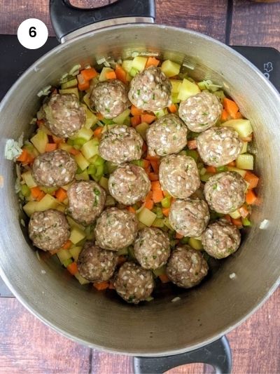 Placing the meatballs in the pot on top of the veggies.