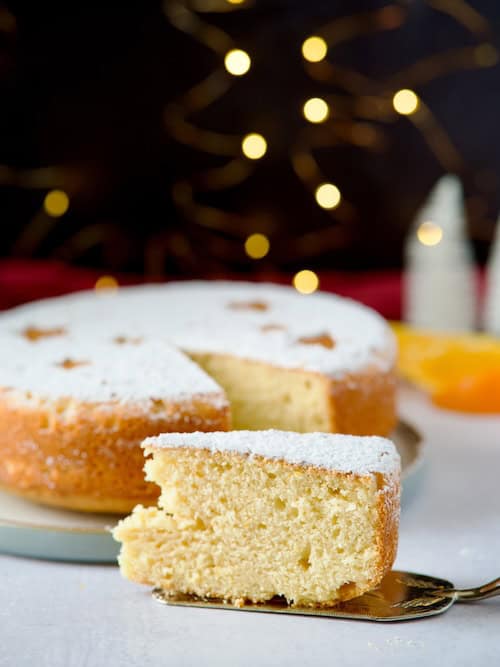 Greek new year cake decorated with powdered sugar and year date and one slice cut and served on a grey plate.