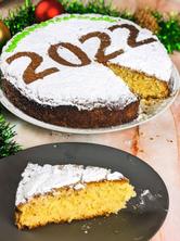 Greek new year cake decorated with powdered sugar and year date and one slice cut and served on a grey plate.