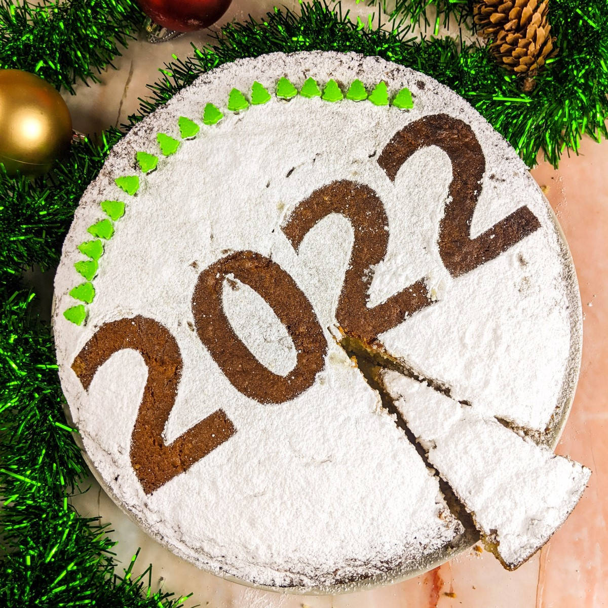 Greek new year cake decorated with powdered sugar and year date and one slice cut and served on a grey plate.