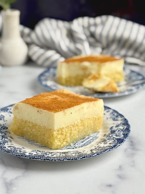 A square slice of semolina and cream dessert served on blue porcelain dish.