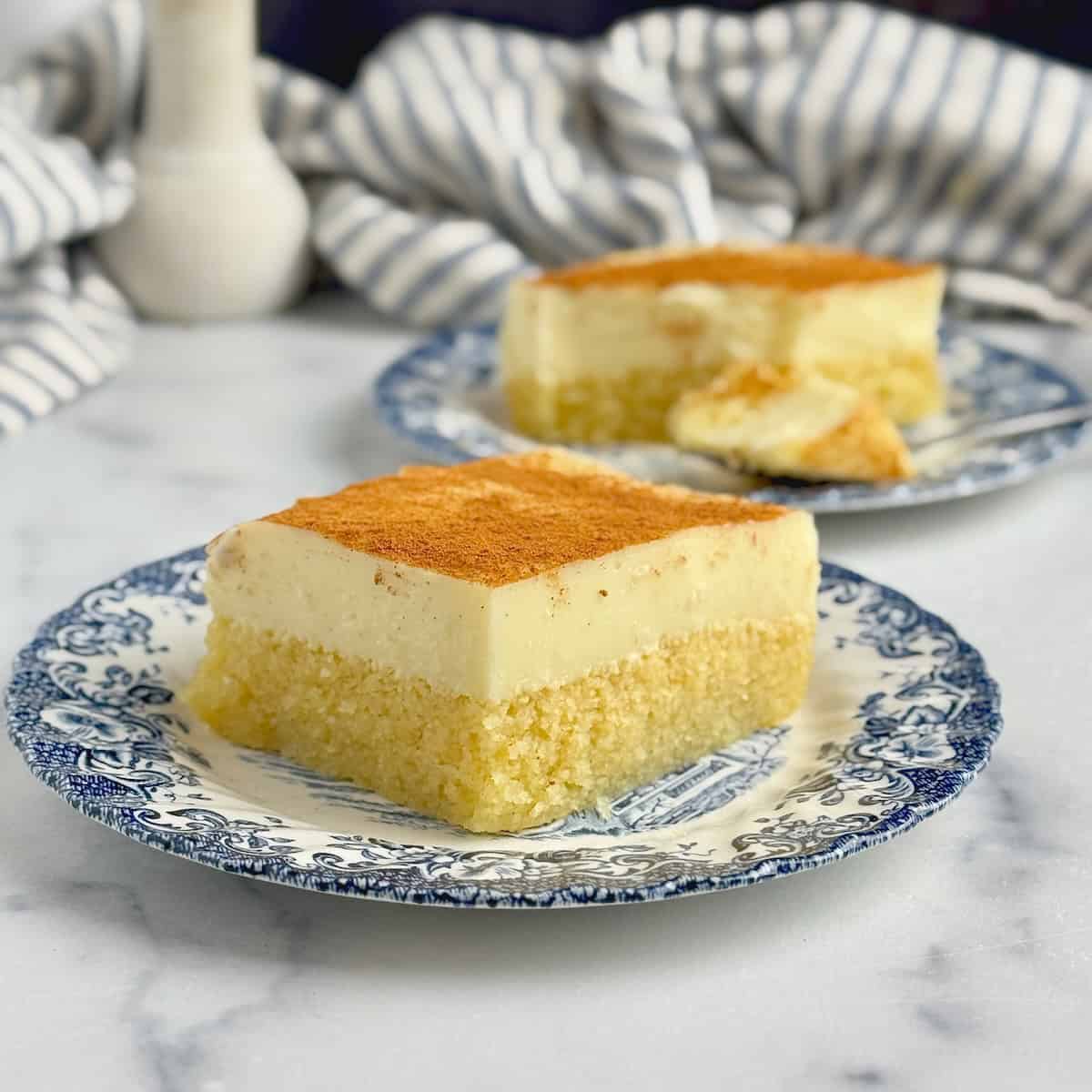 A square slice of semolina and cream dessert served on blue porcelain dish.