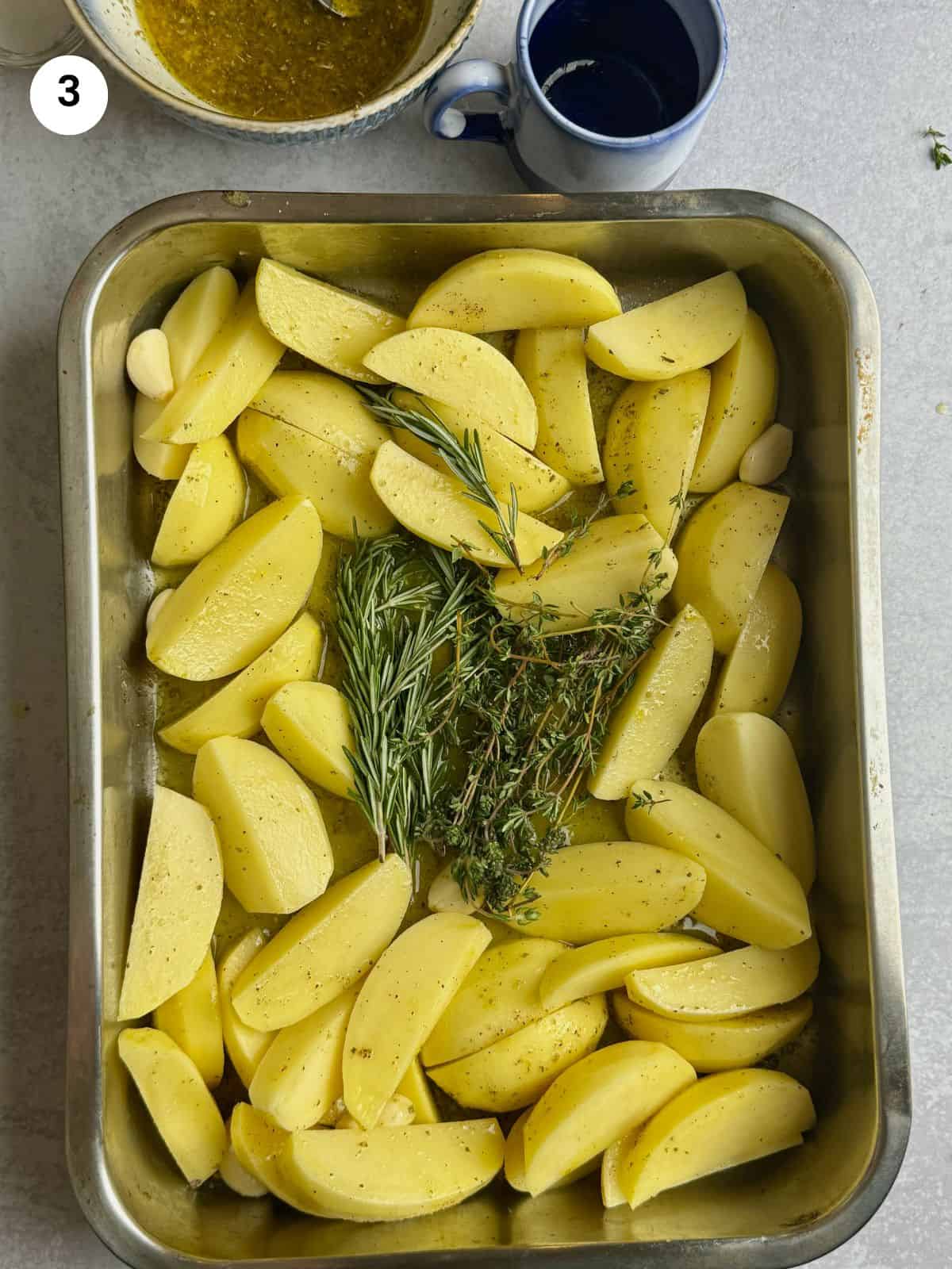 Placing the thyme and rosemary in the middle of the tray between the potatoes.