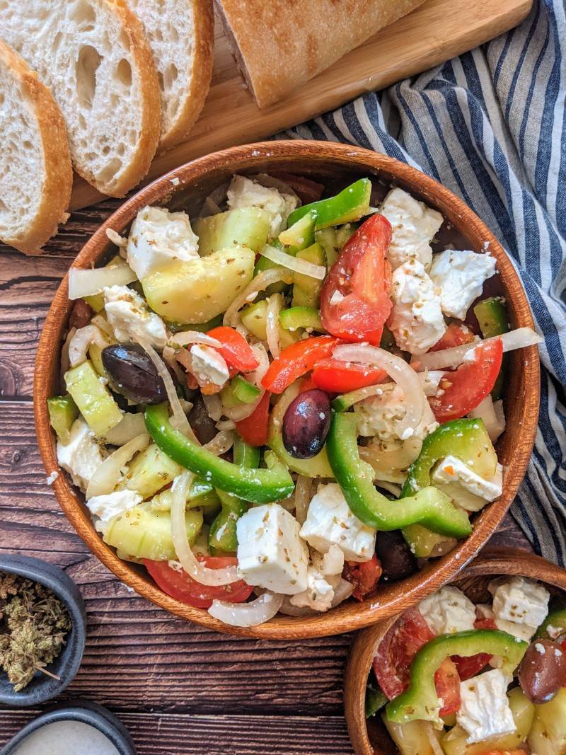 Greek salad served in wooden bowl next to some bread slices