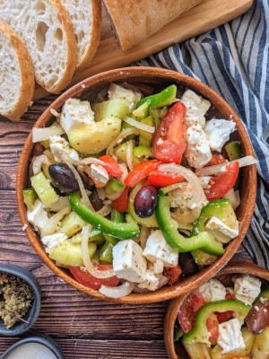 Greek Salad served in wooden bowl next to a loaf of bread