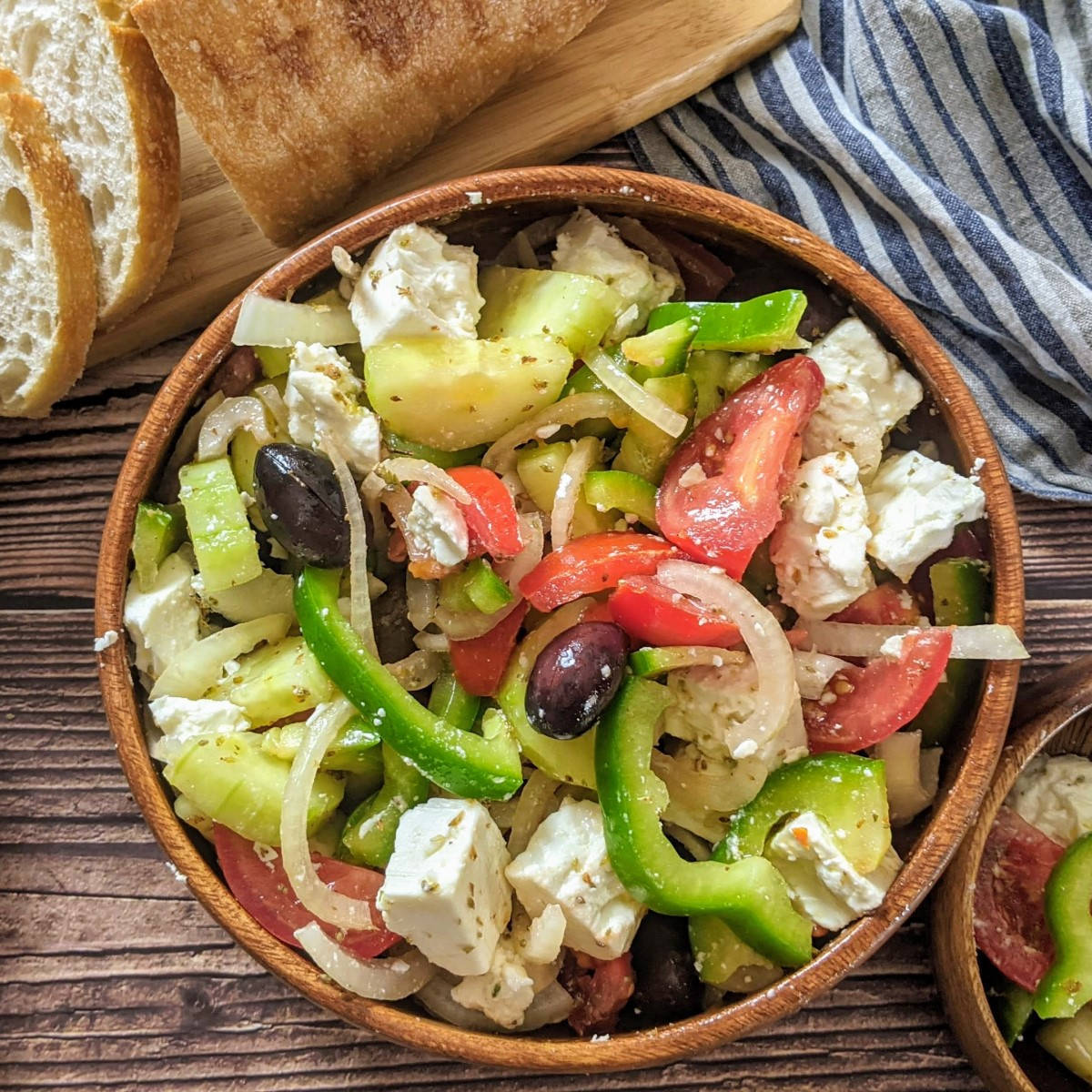 Greek Salad served in wooden bowl next to a loaf of bread