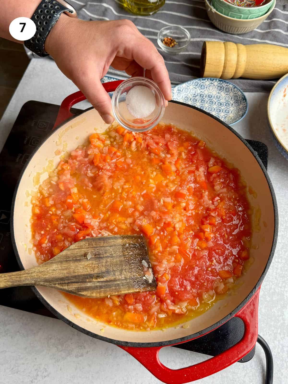 Adding salt to the tomato sauce.