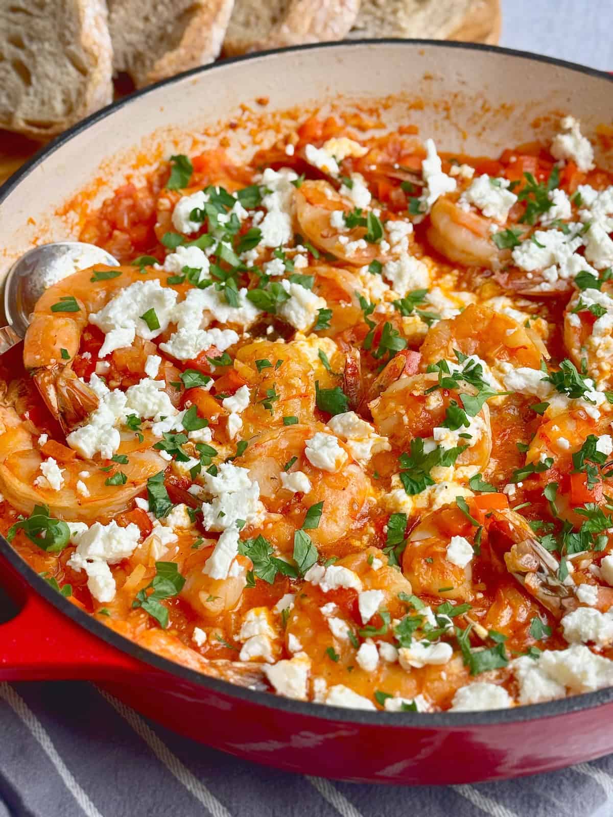 Shrimp saganaki in a red pan with chopped parsley on top.