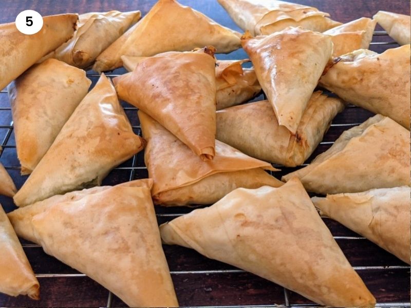 Spinach & feta cheese triangles cooling down on a wire rack.