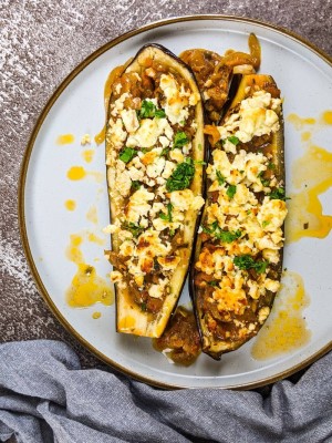 Two stuffed eggplants served on a plate with fresh parsley on top.
