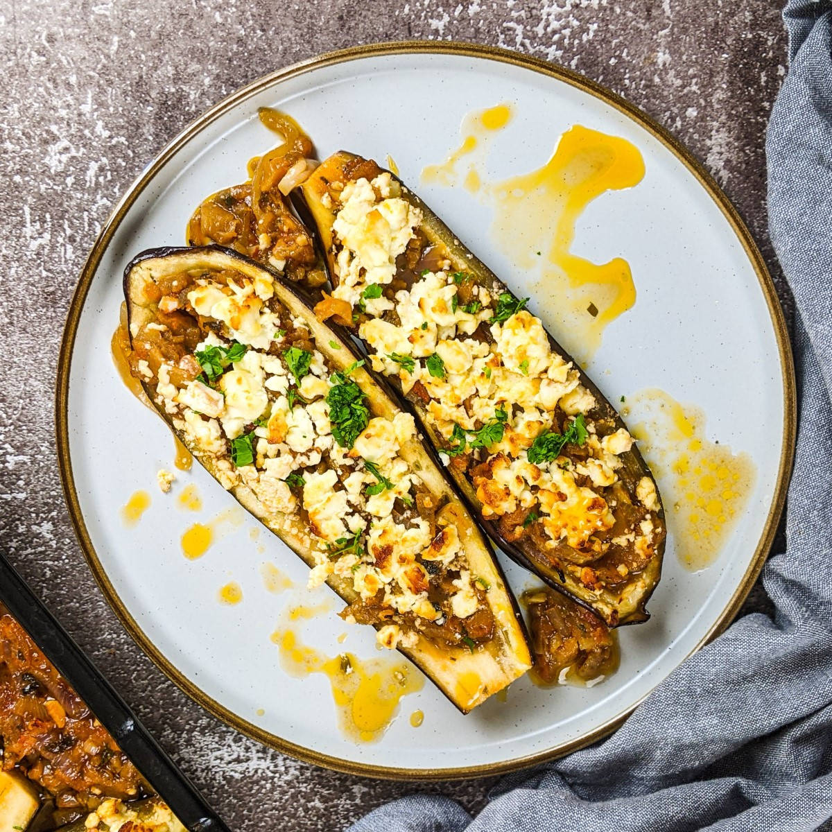 Two stuffed eggplants served on a plate with fresh parsley on top.