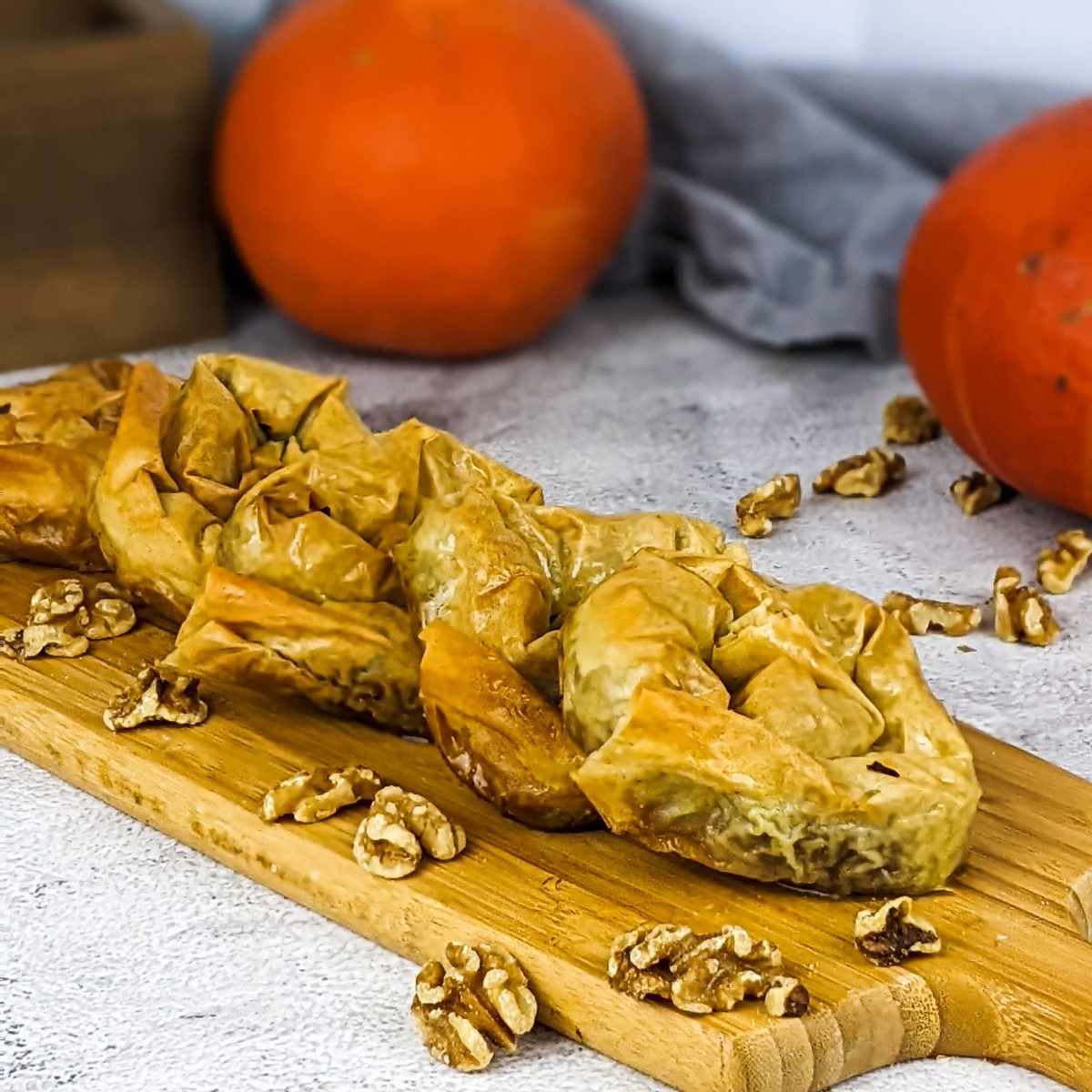 Greek sweet pumpkin pies on a wooden tray next to orange squash.