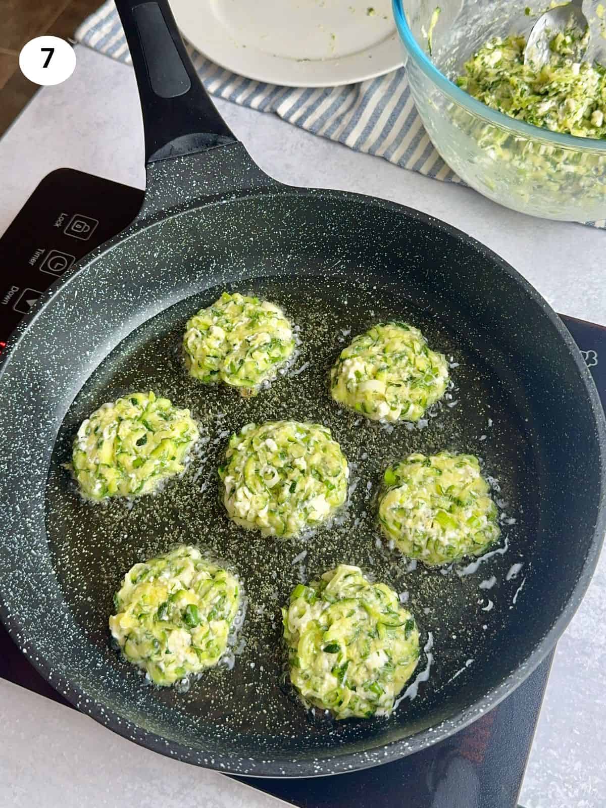 Zucchini fritters in a pan cooking on one side.