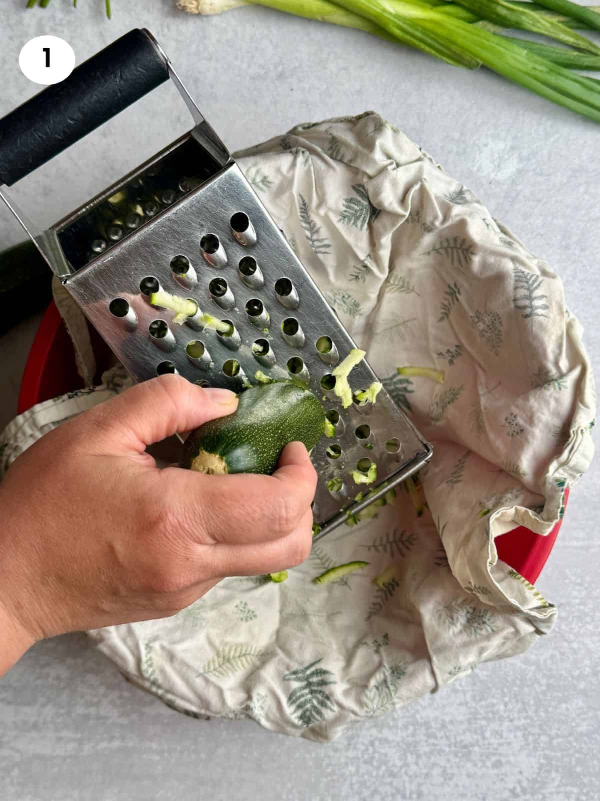Grating zucchinis in a glass bowl on top of a towel.