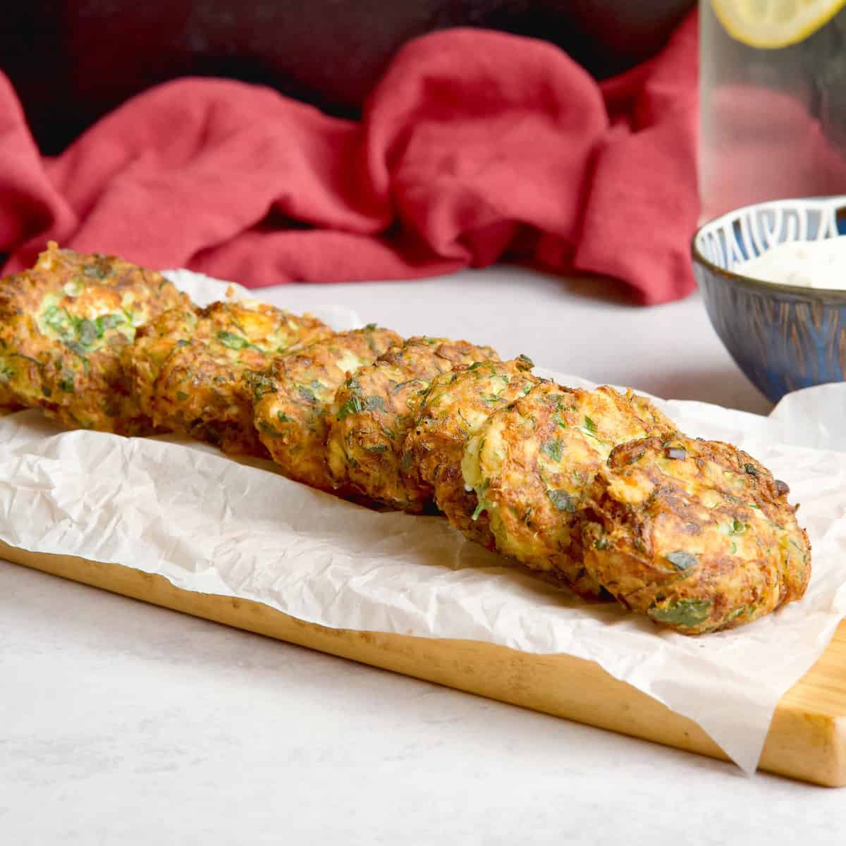 Zucchini fritters layed on a wooden board next to a yogurt dip.