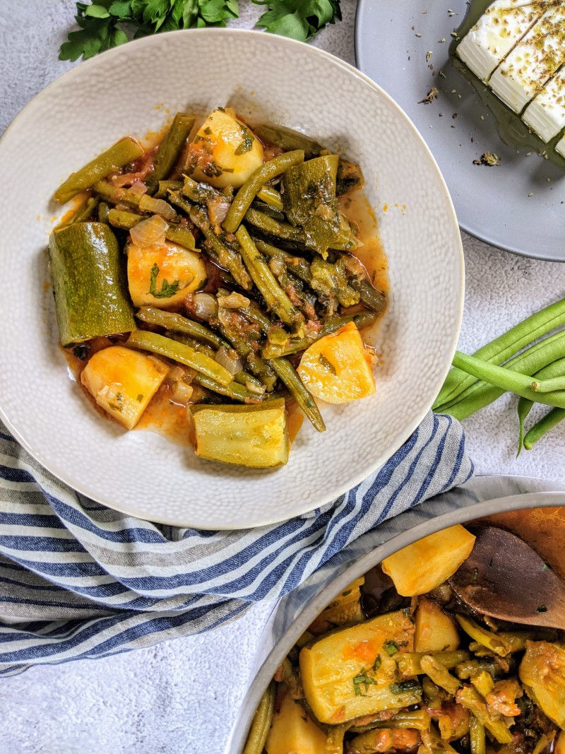 Green beans stew served in a bowl next to a bunch of parsley, a handful of green beans and a blue st