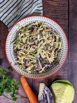 Coleslaw salad served in a bowl with a carrot and red, green cabbage next to the bowl