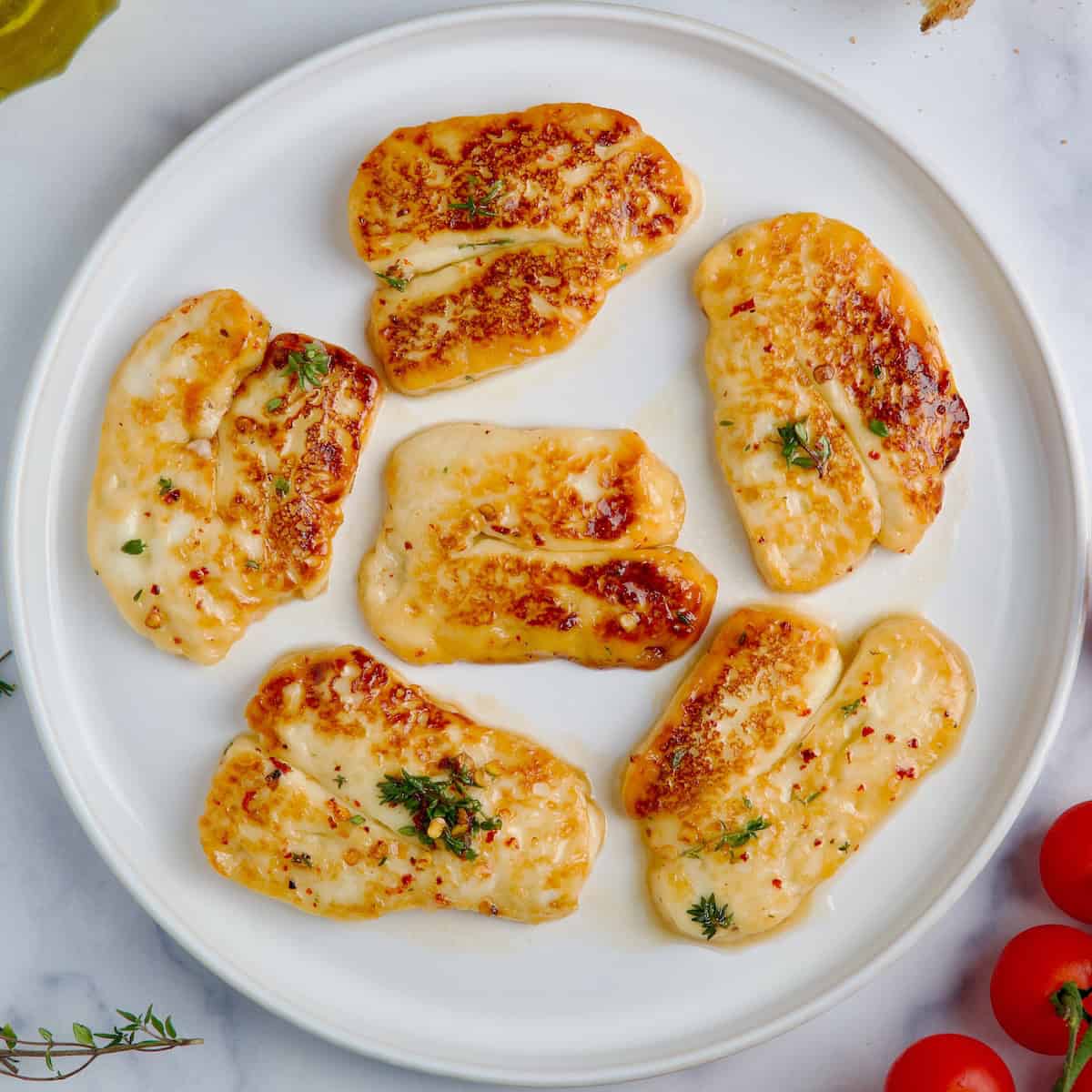 Fried halloumi slices on a white plate next to cherry tomatoes and thyme sprigs.
