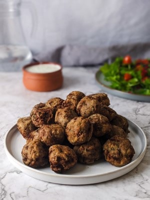 Keftedakia meatballs served on a white plate with tzatziki dip at the back and greens salad.