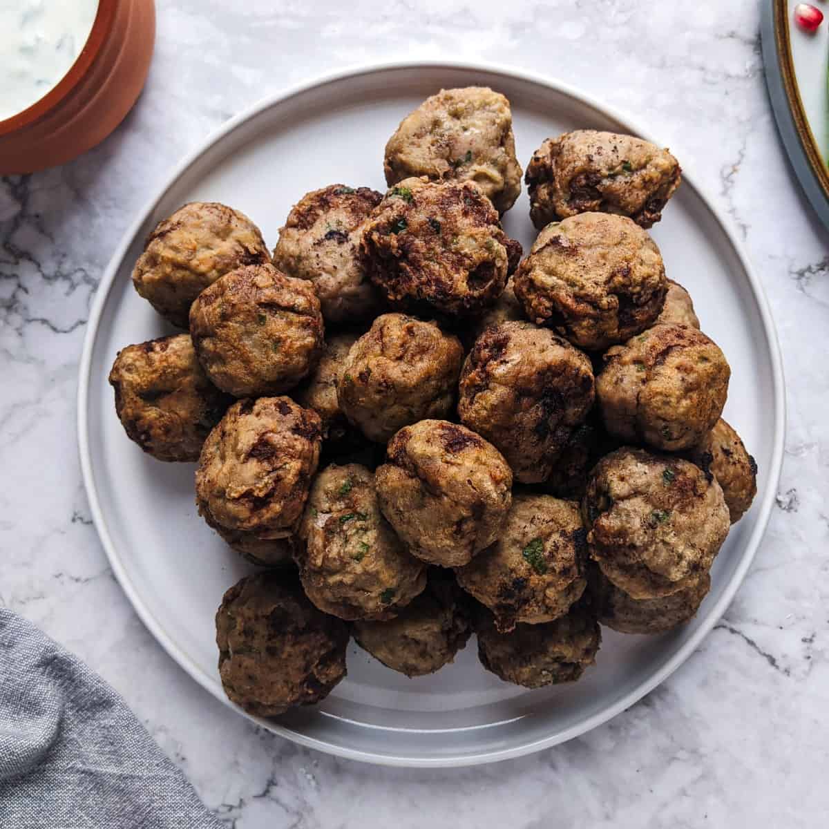 Keftedakia meatballs served on a white plate with tzatziki dip at the back and greens salad.