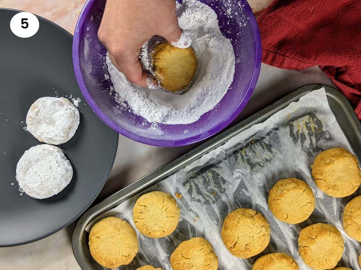 Covering a greek butter cookie with powdered sugar and putting it on a serving plate.