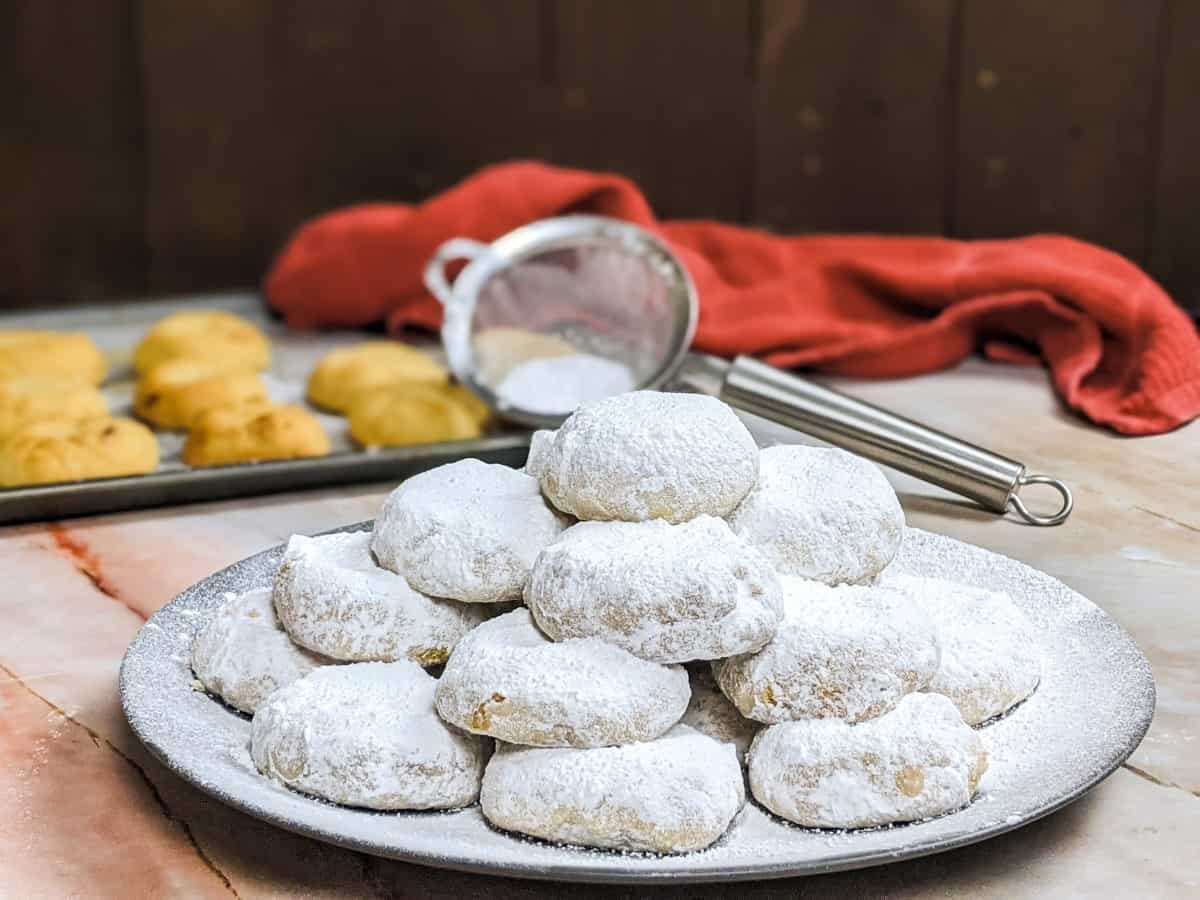 Kourabiedes served on a plate with powdered sugar on.