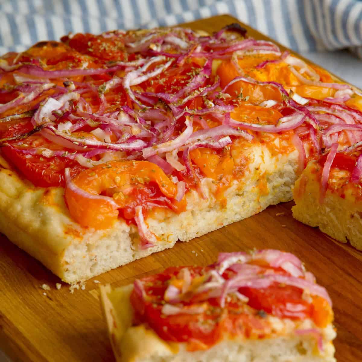 Greek flatbread on a wooden board with three slices cut at the front.