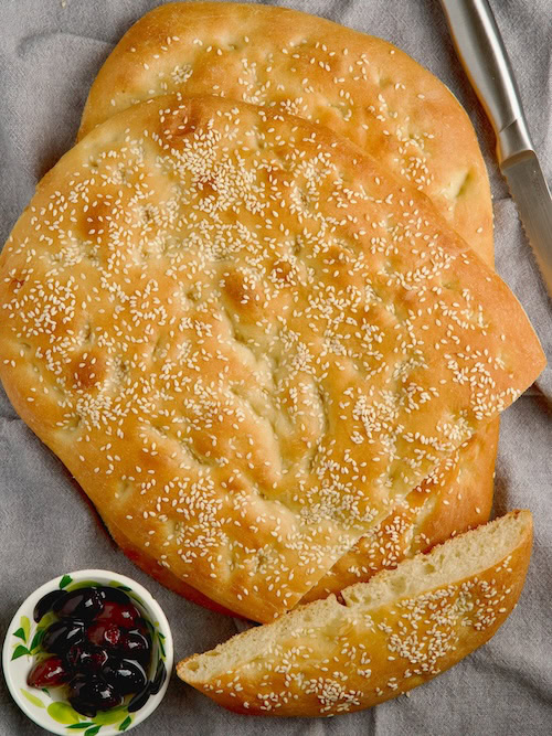 Two lagana breads, one on top of each other with a bowl with olives on the side.
