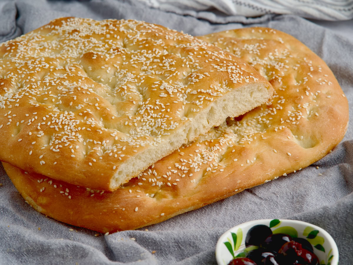 Greek olive bread on a wooden board next to olive oil bottle and olives.