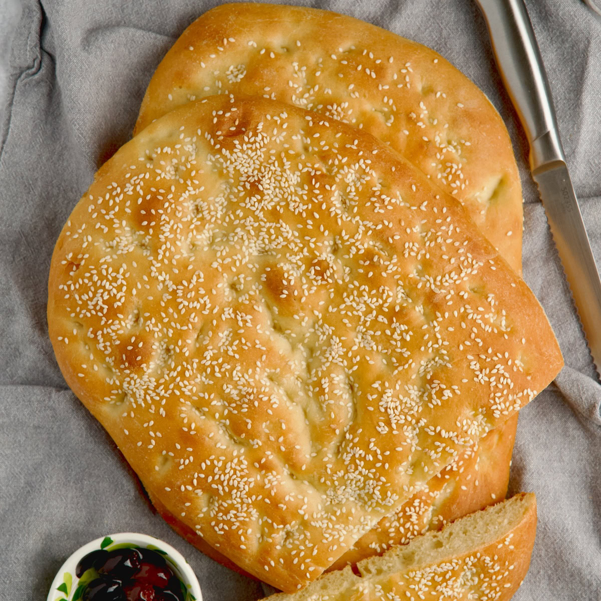 Two lagana breads, one on top of each other with a bowl with olives on the side.