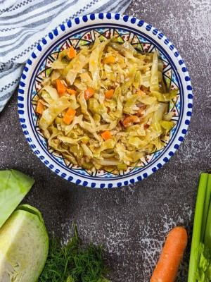 Cabbage and rice stew served on a plate next to cabbage, carrot and celery.