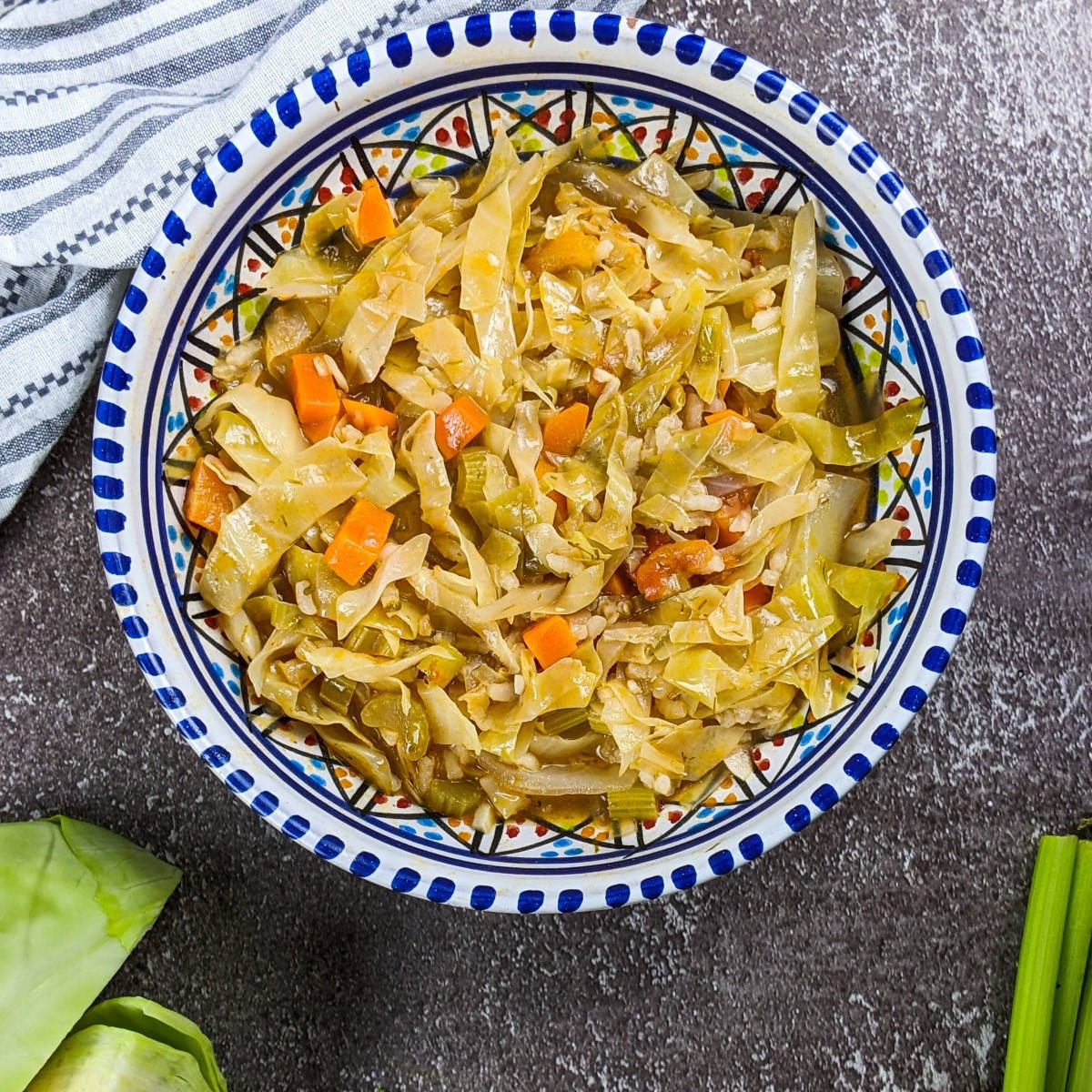 Cabbage and rice stew served on a plate next to cabbage, carrot and celery.