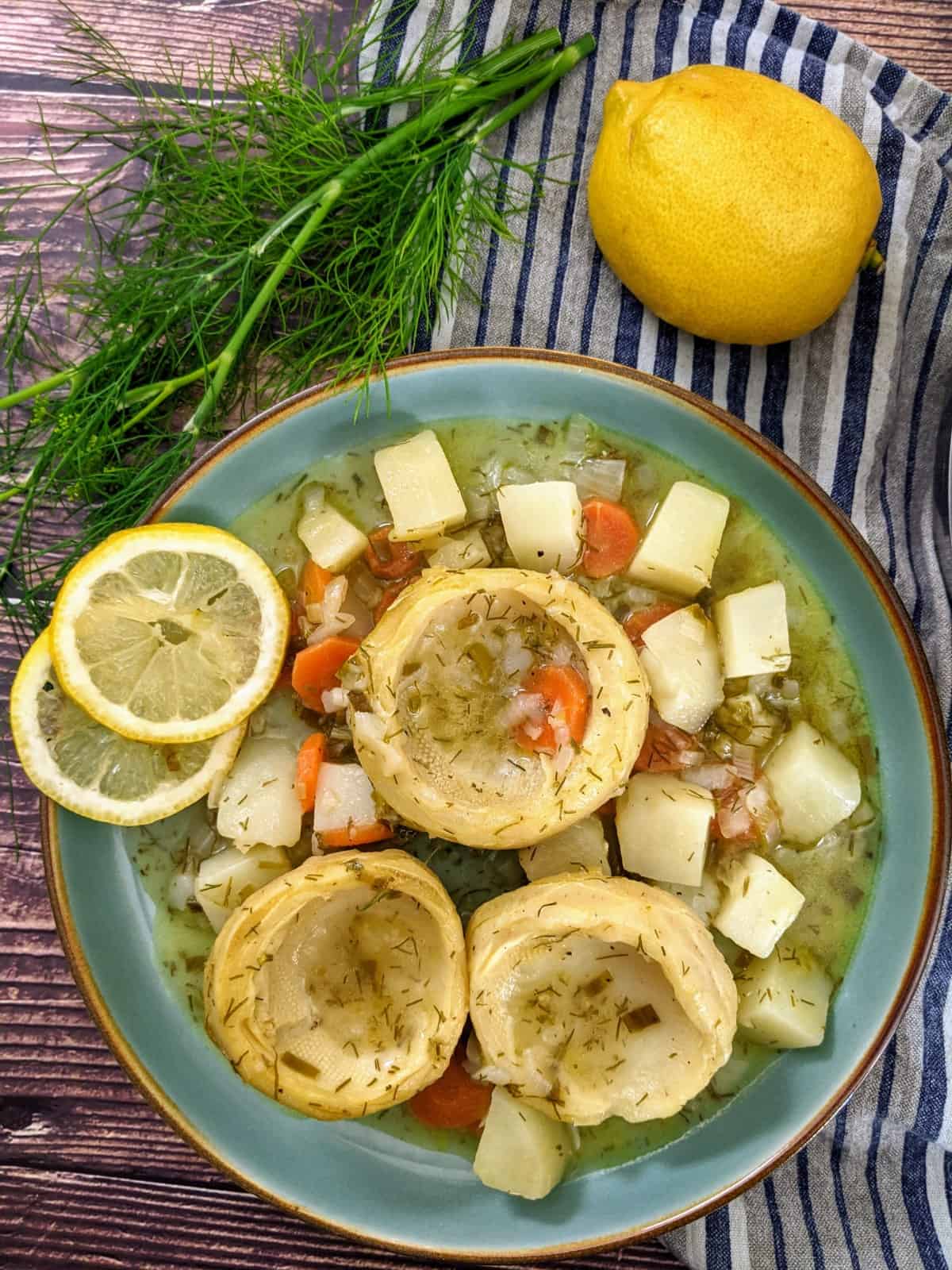 Artichoke stew served on blue plate next to some dill and a lemon